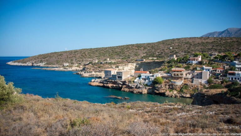 Small coastal village of white and stone houses gathered around a sheltered blue cove.