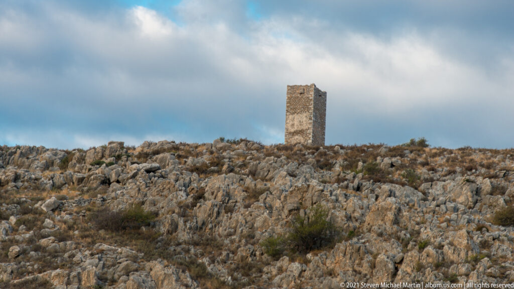 Isolated rectangular stone tower standing on a pale rocky ridge beneath a cloudy sky.