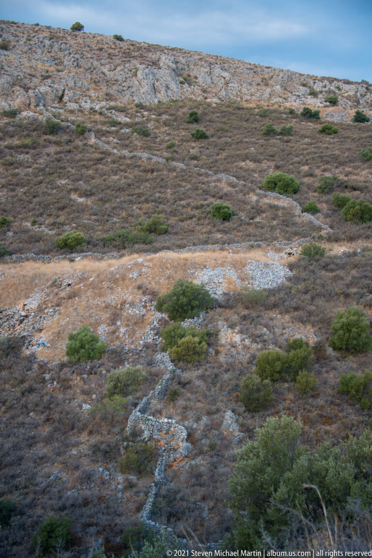 Pale weathered rock stretches across low terrain dotted with scattered rounded green shrubs.
