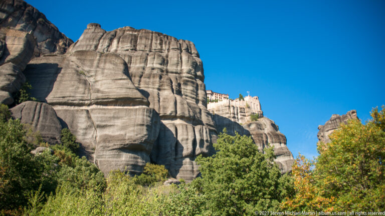 Large monastery complex high on the skyline behind massive rounded and grooved sandstone buttresses.