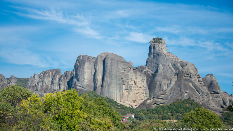 Cluster of towering gray sandstone pillars above green woodland, with a small red-roofed building near the base.