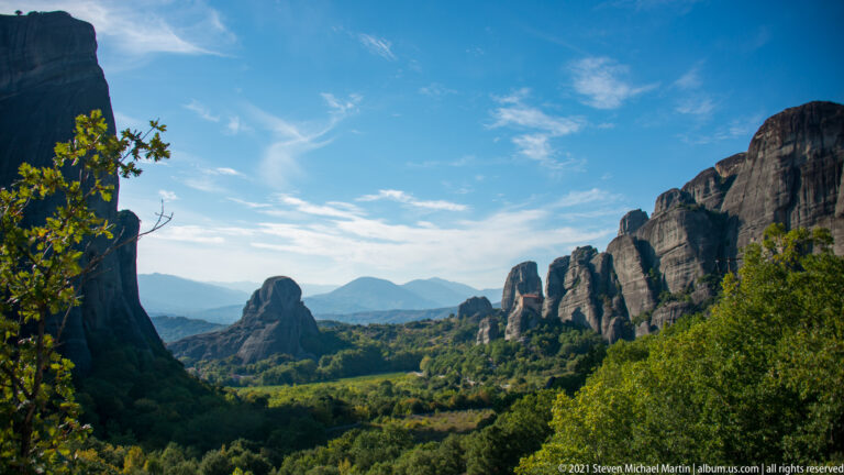 Sandstone pillars rise above a densely wooded valley, with layered mountain ridges fading into the distance.