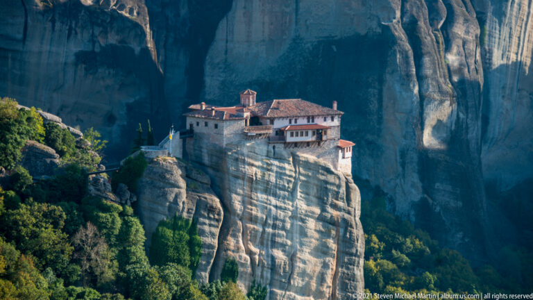 Stone monastery with red tile roofs and a small chapel sits on a steep, striated sandstone pillar.