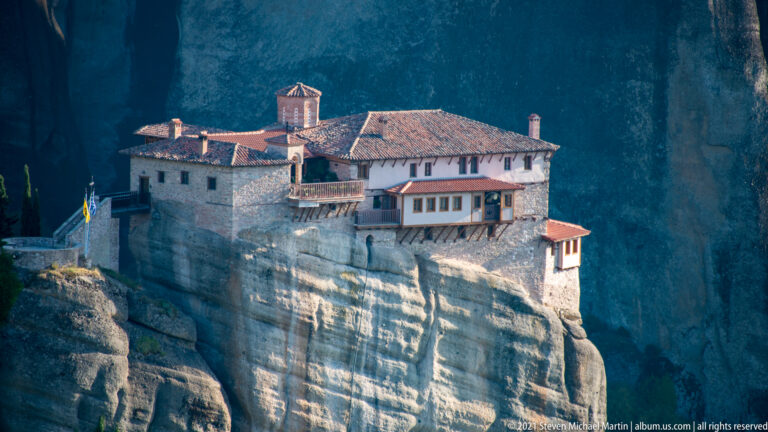 Close view of stone monastery buildings with red tiled roofs and a small chapel perched on a sandstone summit.