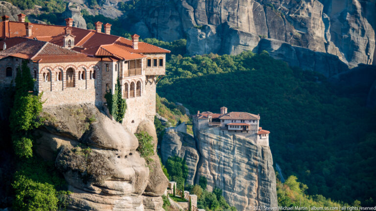 Arcaded stone monastery fills the left foreground while a second monastery stands on a separate rock pillar beyond.