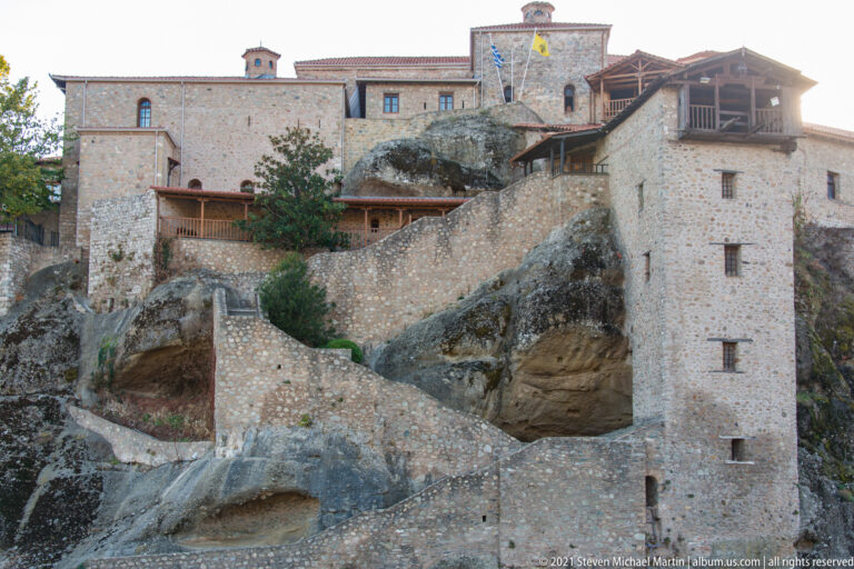 Stone monastery buildings, terraces, and stairways are fitted around large exposed masses of natural bedrock.