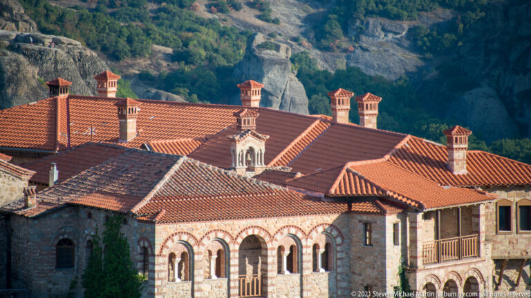Red tiled monastery roofs, multiple chimneys, and arched stone-and-brick openings seen in a tight architectural view.