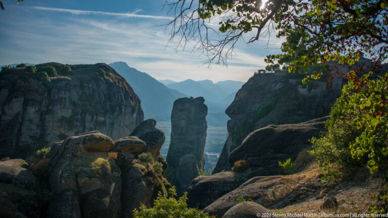 Central sandstone spire is framed by rounded rocks and autumn foliage, with distant mountains under a pale sky.