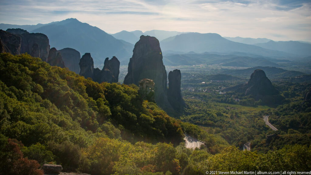 Dark sandstone pinnacles rise above wooded slopes and a broad valley backed by hazy mountain ridges.