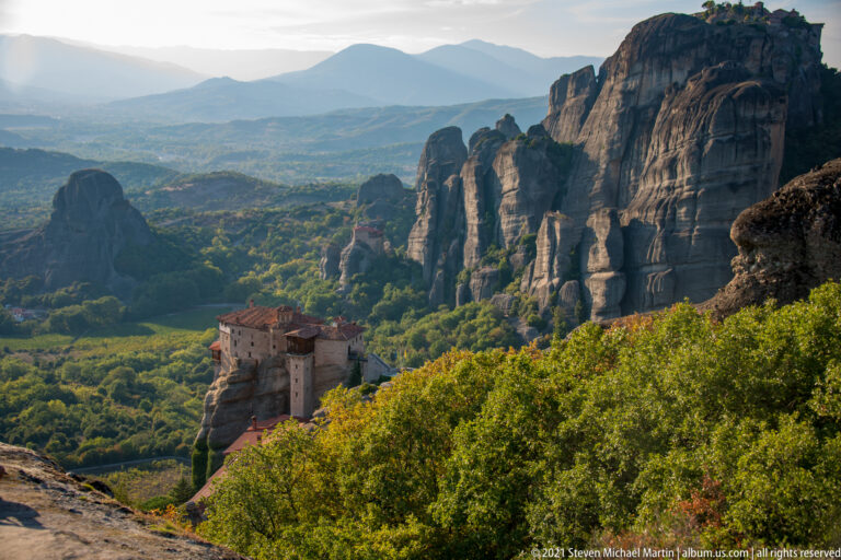 Foreground monastery and distant summit complex sit among tall sandstone towers and dense green woodland.