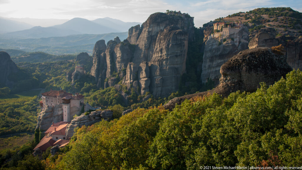 Monastery sits low among dense trees beneath a long line of towering sandstone cliffs and pinnacles.