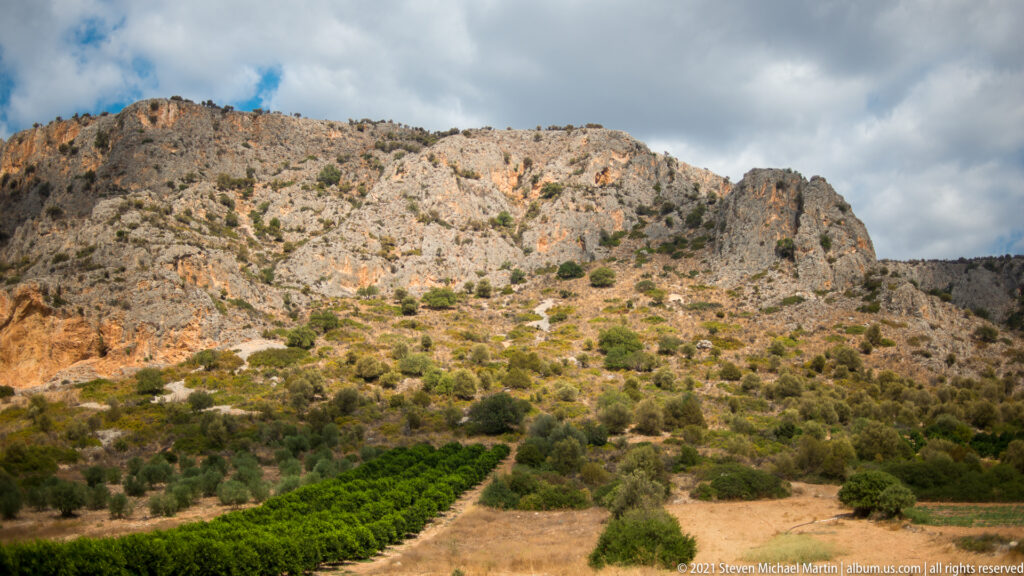 Rocky limestone hillside with scrub vegetation above cultivated fields on the lower slopes near Palamidi Fortress.