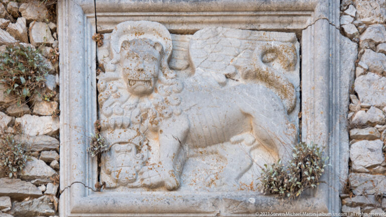 Weathered stone relief of a winged lion carved in profile and set into rough fortress masonry.
