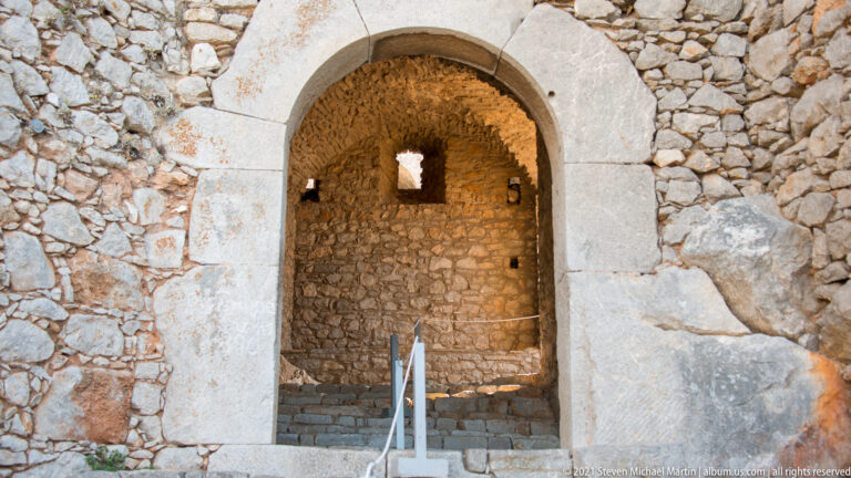 Dressed-stone round arch opening into a small rough-masonry chamber with steps and a rear window.