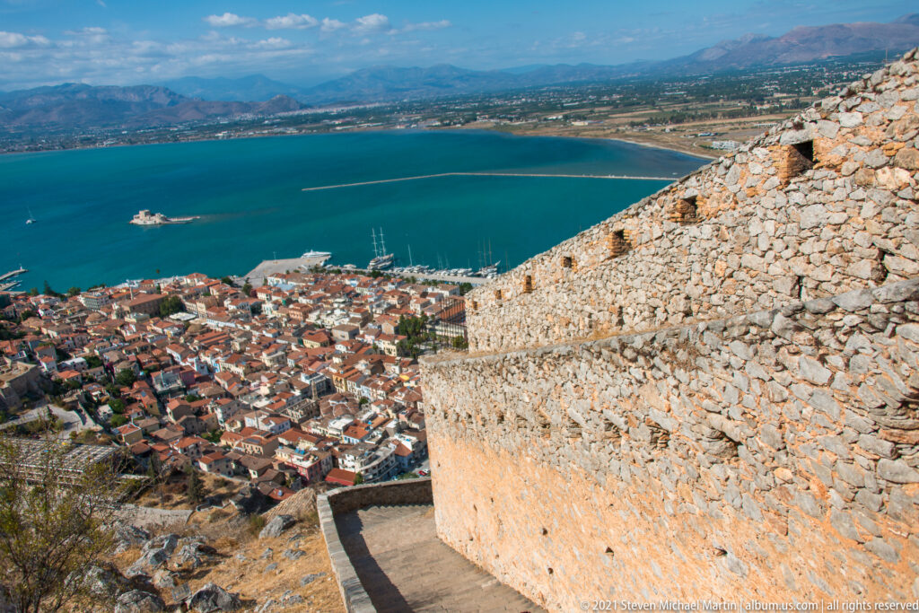 Palamidi rampart above Nafplio, with Bourtzi offshore in the turquoise gulf and mountains beyond.