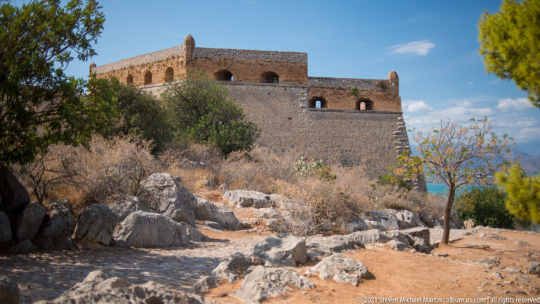 Large angular stone bastion at Palamidi Fortress beyond rocky ground and scattered trees.