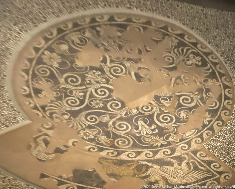 Circular pebble mosaic from Pella with Dionysus riding a panther amid scrolling vegetation, animals, and a patterned border.
