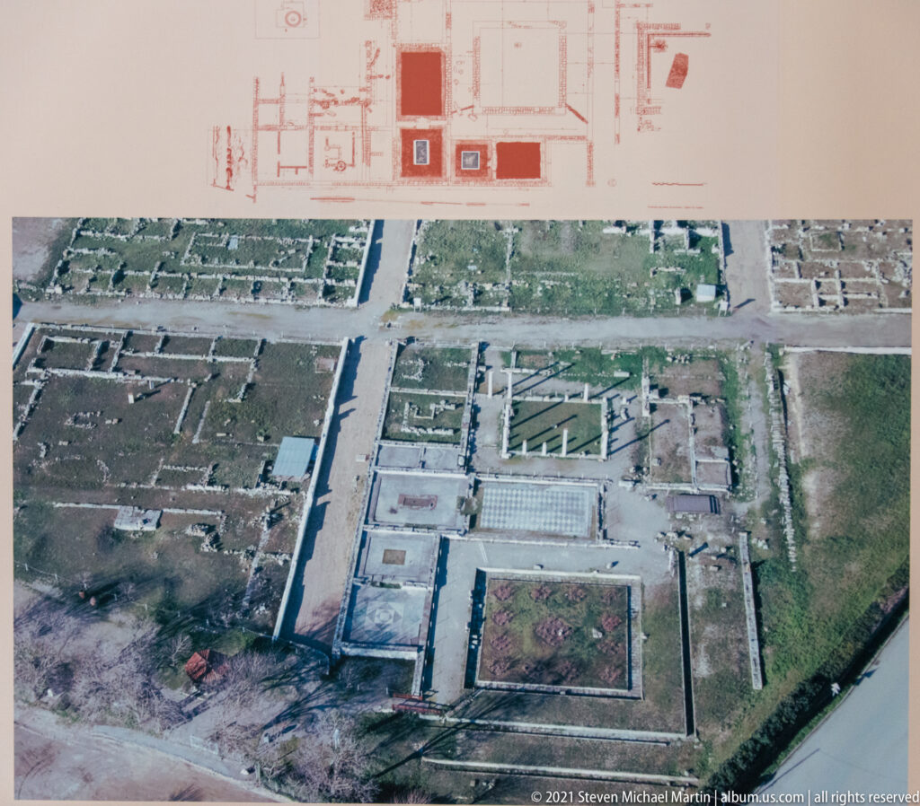 Museum panel with an aerial photograph and plan of excavated rectangular city blocks and streets at Pella.