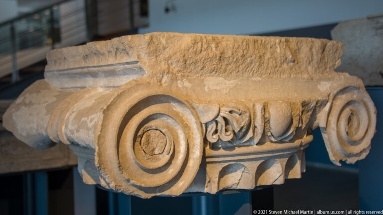 Fragmentary stone Ionic capital with large spiral volutes and carved vegetal ornament across the center.