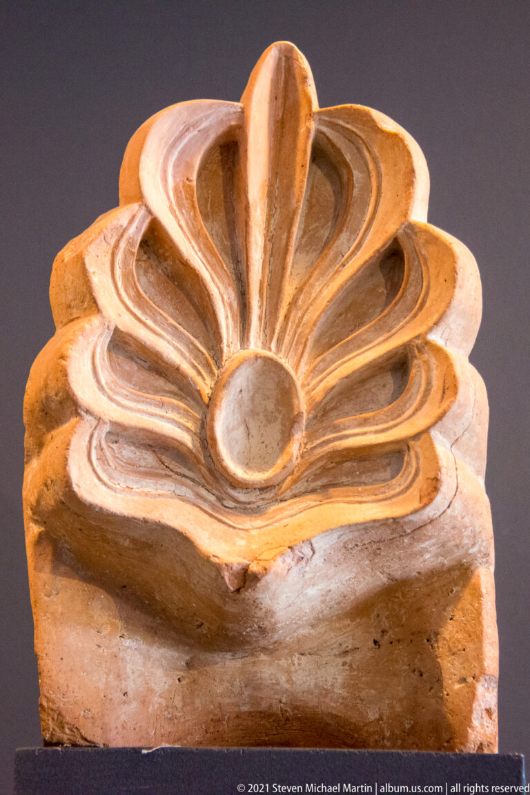 Fan-shaped palmette ornament with a central upright lobe and deeply grooved curling leaves.