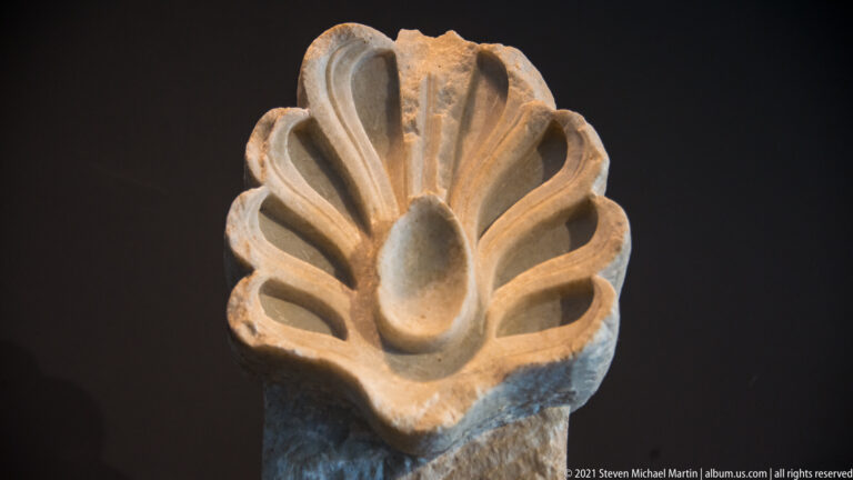 Narrow upright palmette ornament with elongated curling leaves framing a central teardrop-shaped lobe.