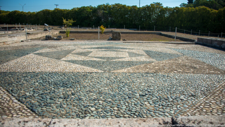 Large in-situ pebble mosaic with dark and light geometric fields surrounded by low excavated walls.