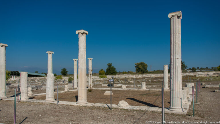 Multiple standing columns, including one tall fluted shaft, among low archaeological foundations.