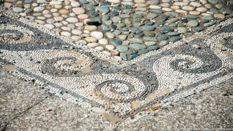 Close detail of pebble mosaic corner with black-and-white spirals, triangular borders, and greenish stones.