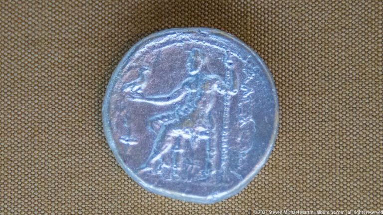 Close-up of a small worn ancient coin showing a standing human figure within a circular border.
