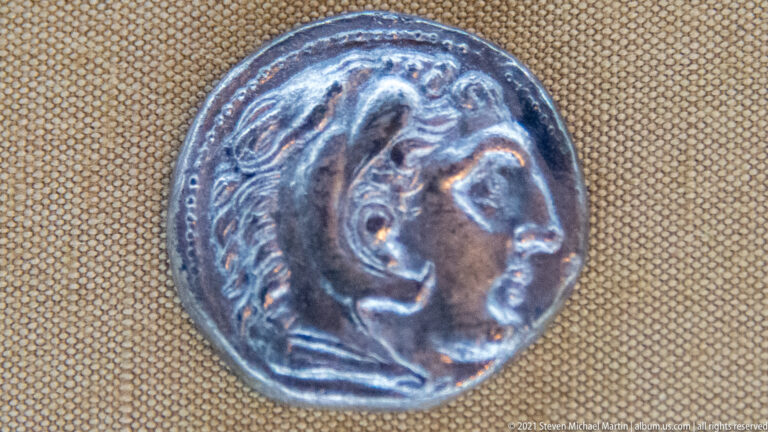 Close-up of a silver-toned ancient coin with a right-facing male portrait head in relief.