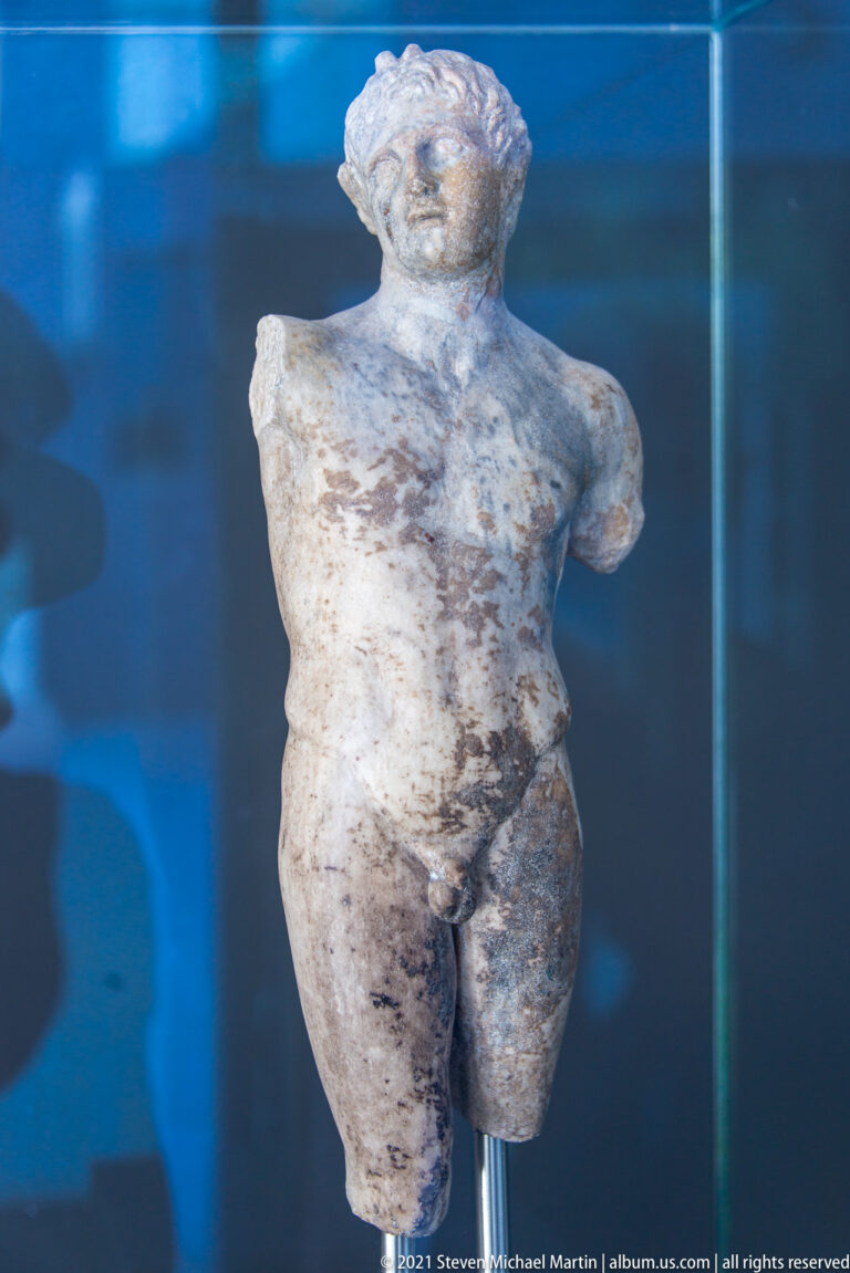 Fragmentary marble statuette of a nude male figure, missing both arms and the lower legs.
