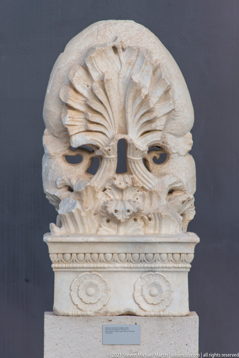 Carved marble palmette above a rectangular block with bead molding and paired rosettes.