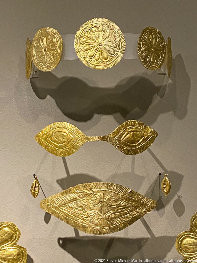 Embossed gold rosette plaques and elongated patterned bands mounted against a gray museum wall.