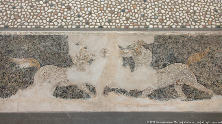 Fragmentary pebble mosaic with a pale horse and partial human figures preserved within a rectangular panel.