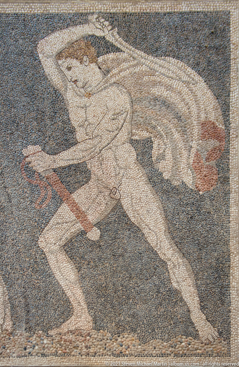 Winged human figure running across a dark pebble mosaic while holding a long reddish object.