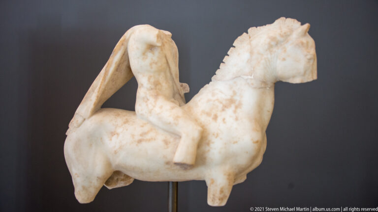 Fragmentary marble statuette of a horse with the lower body and drapery of a rider preserved.