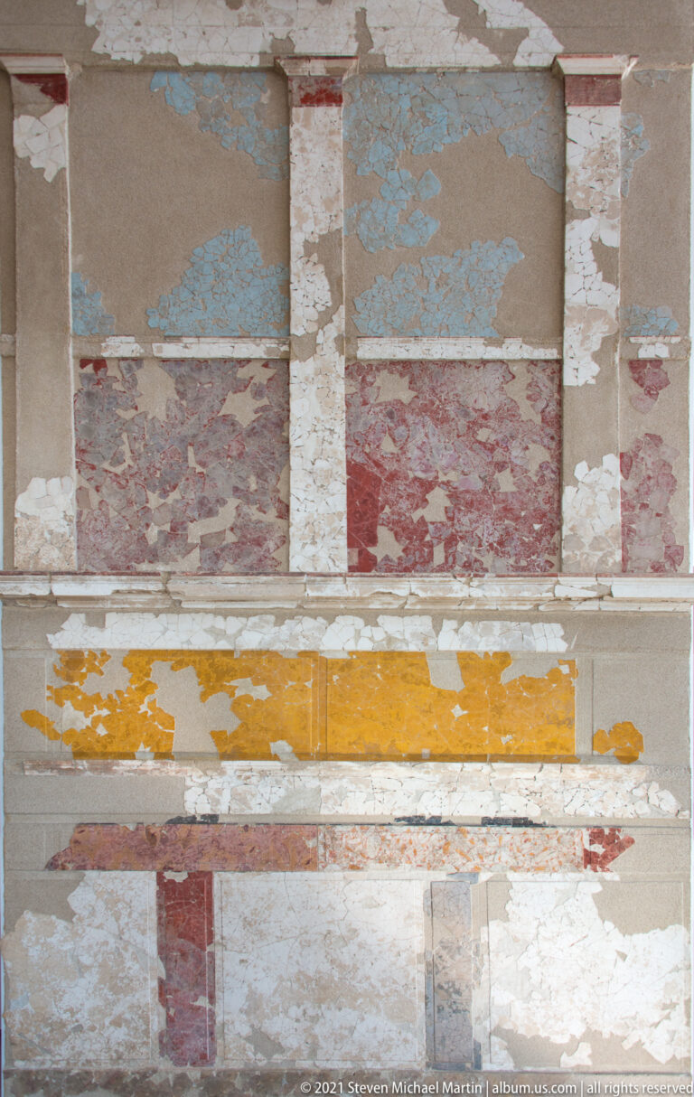 Fragmentary painted plaster wall with red, blue, yellow, and white rectangular panels imitating masonry.