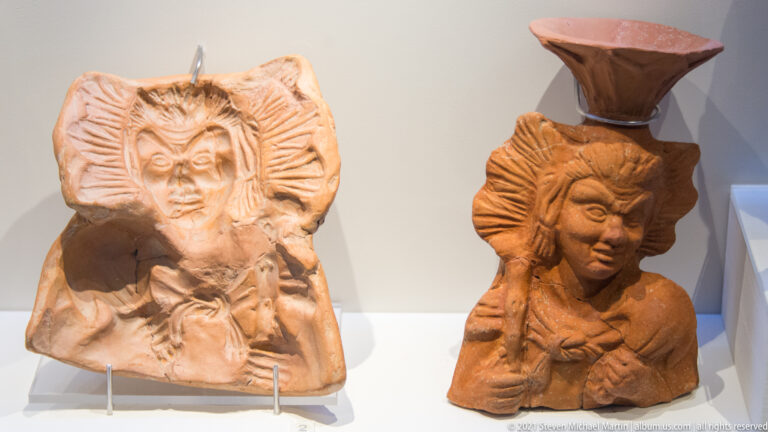 Two terracotta female busts with elaborate headdresses, one larger and fan-framed, the other supporting a small vessel.