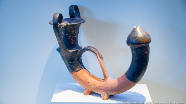 Curved zoomorphic ceramic vessel with a pale horn-like body, dark-painted terminals, and an elongated animal head.