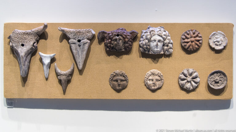 Pointed animal-head fittings, small human faces, and circular rosette ornaments arranged on a rectangular display board.
