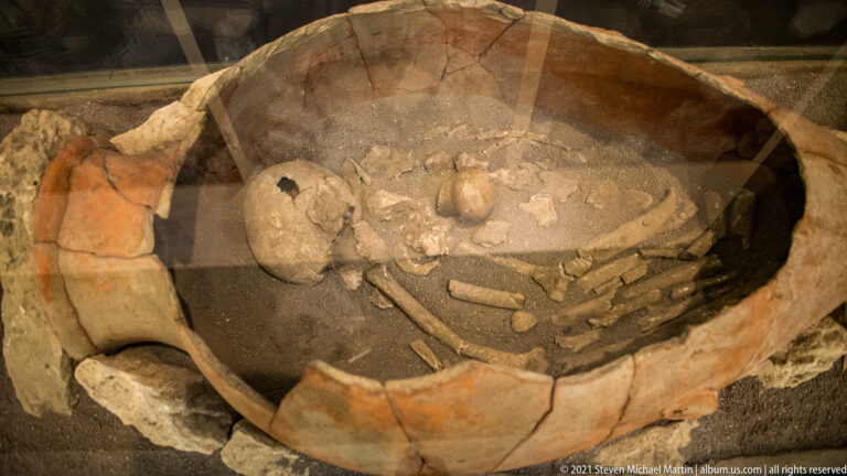 Human skull, ribs, and other bones preserved inside the broken walls of a large ceramic vessel.