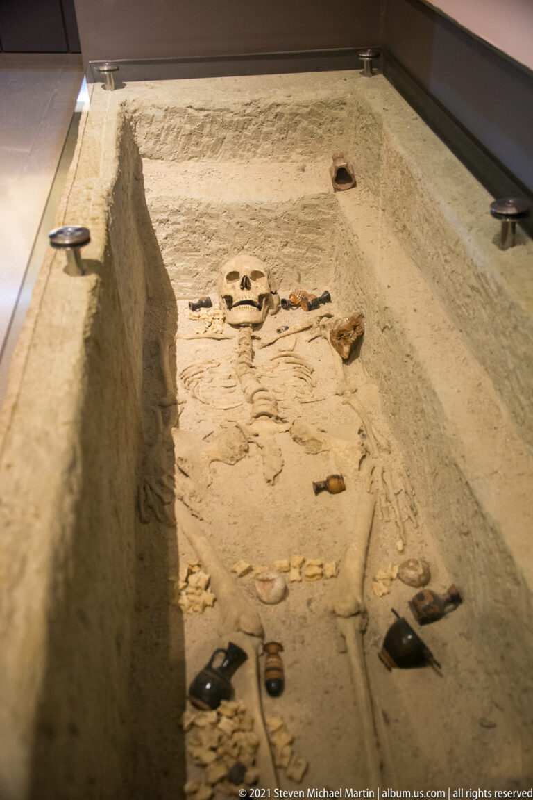 Extended human skeleton lying in a rectangular grave display with small grave goods arranged around the body.