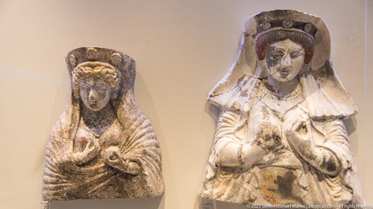 Two draped female figurines with tall headdresses and hands raised near the chest.