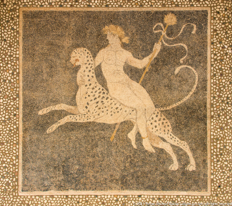 Pebble mosaic of Dionysus riding a spotted panther, framed by a broad field of pale stones.