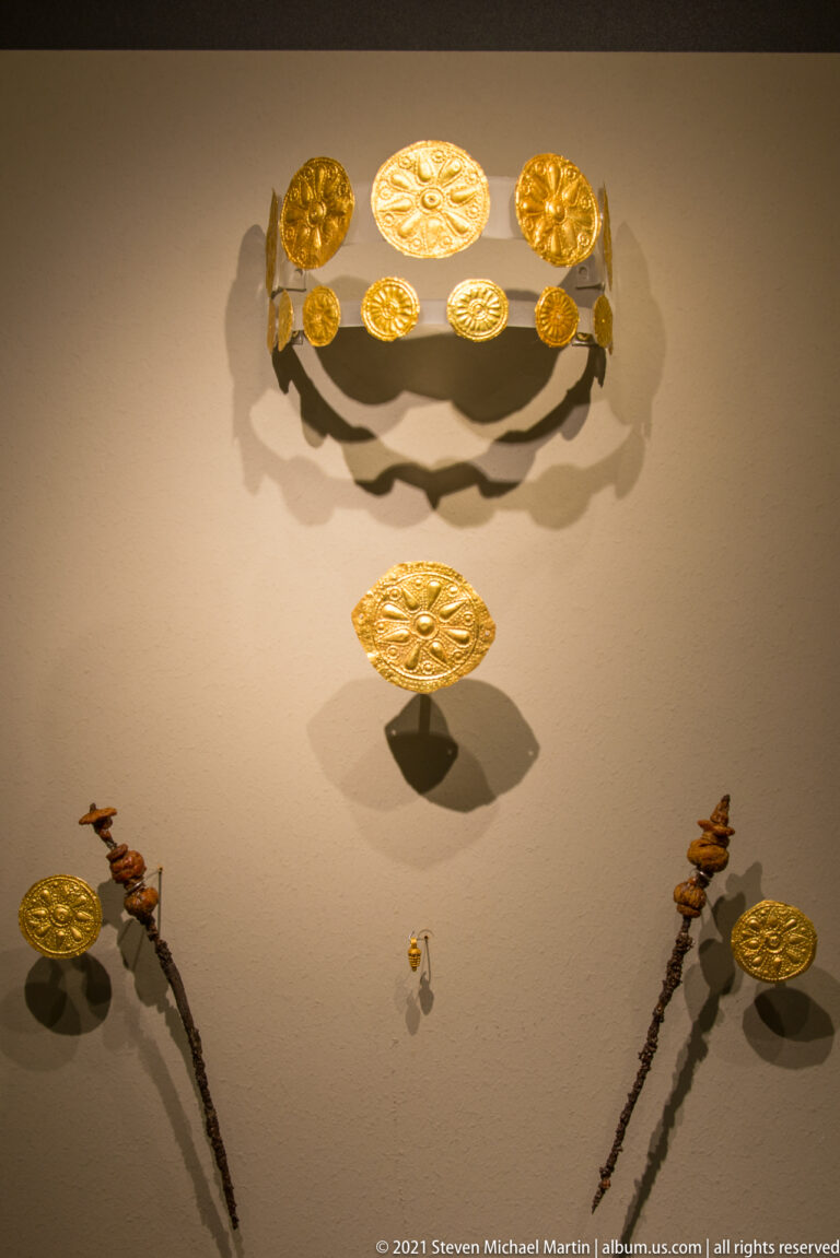 Curved row of embossed gold disks above an oval plaque and paired hanging ornaments.