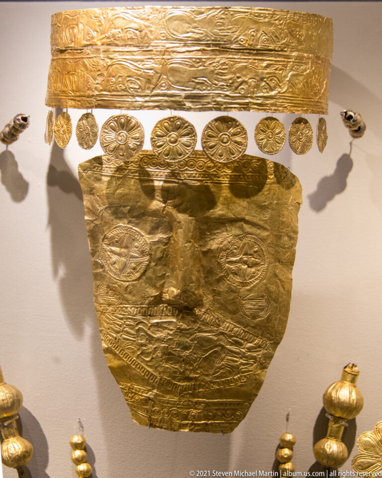 Gold face covering below a broad embossed strip and a row of circular rosettes in a museum display.