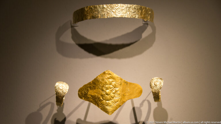 Curved embossed gold band above a diamond-shaped plaque and two smaller spiral-ended gold fittings.