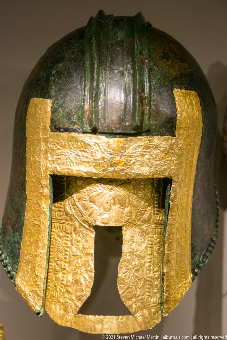 Green-patinated bronze helmet with broad gold bands and an embossed gold panel framing the front opening.
