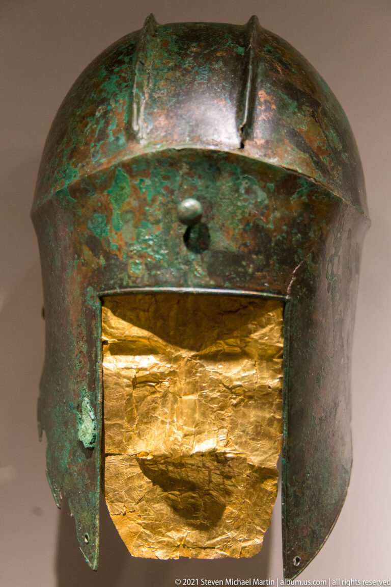 Green-patinated bronze helmet with a large creased sheet-gold plate covering much of the lower front opening.