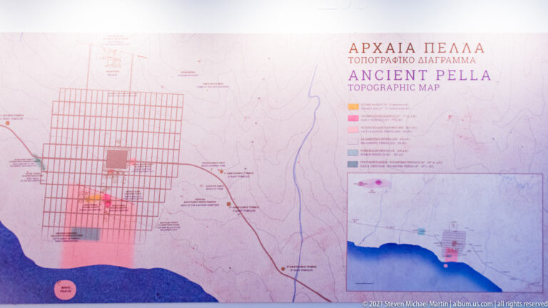 Interpretive topographic map labeled “Ancient Pella,” showing a large rectilinear street grid, colored site zones, roads, and surrounding landscape.